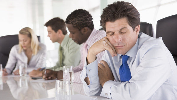 A man dozing at a conference table in the middle of a meeting while three colleagues around him keep working.