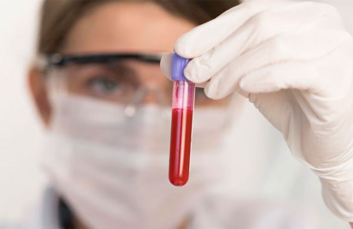 Person in protective gear holding a test tube with red liquid