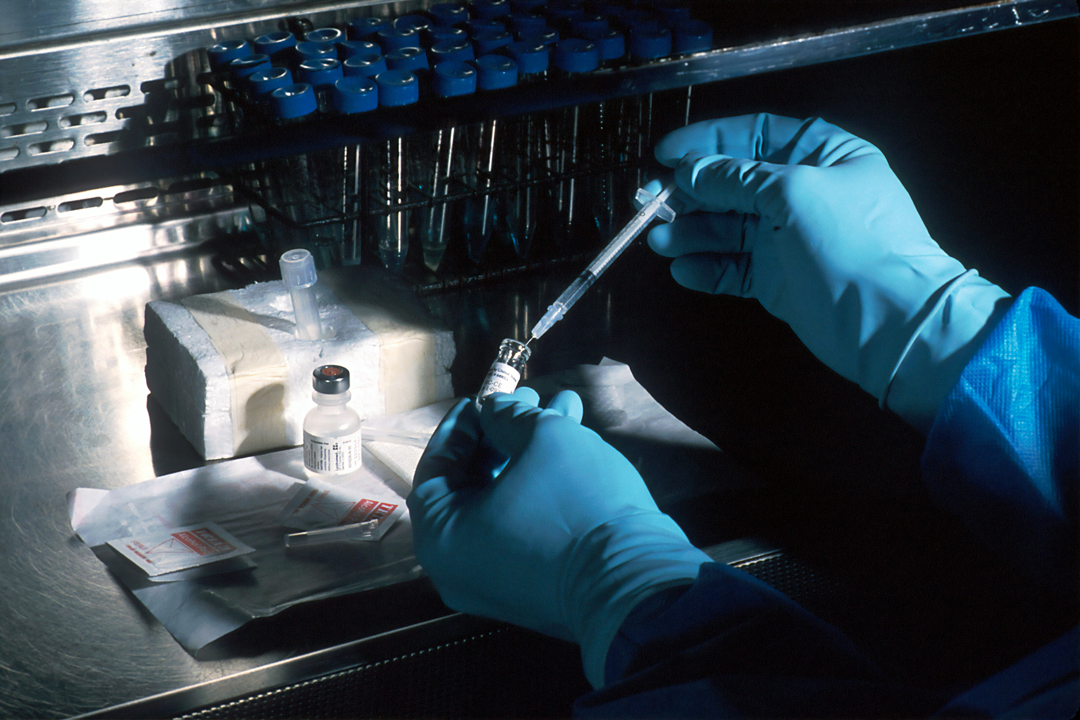 Person in blue gloves handling a syringe and vials in a laboratory setting