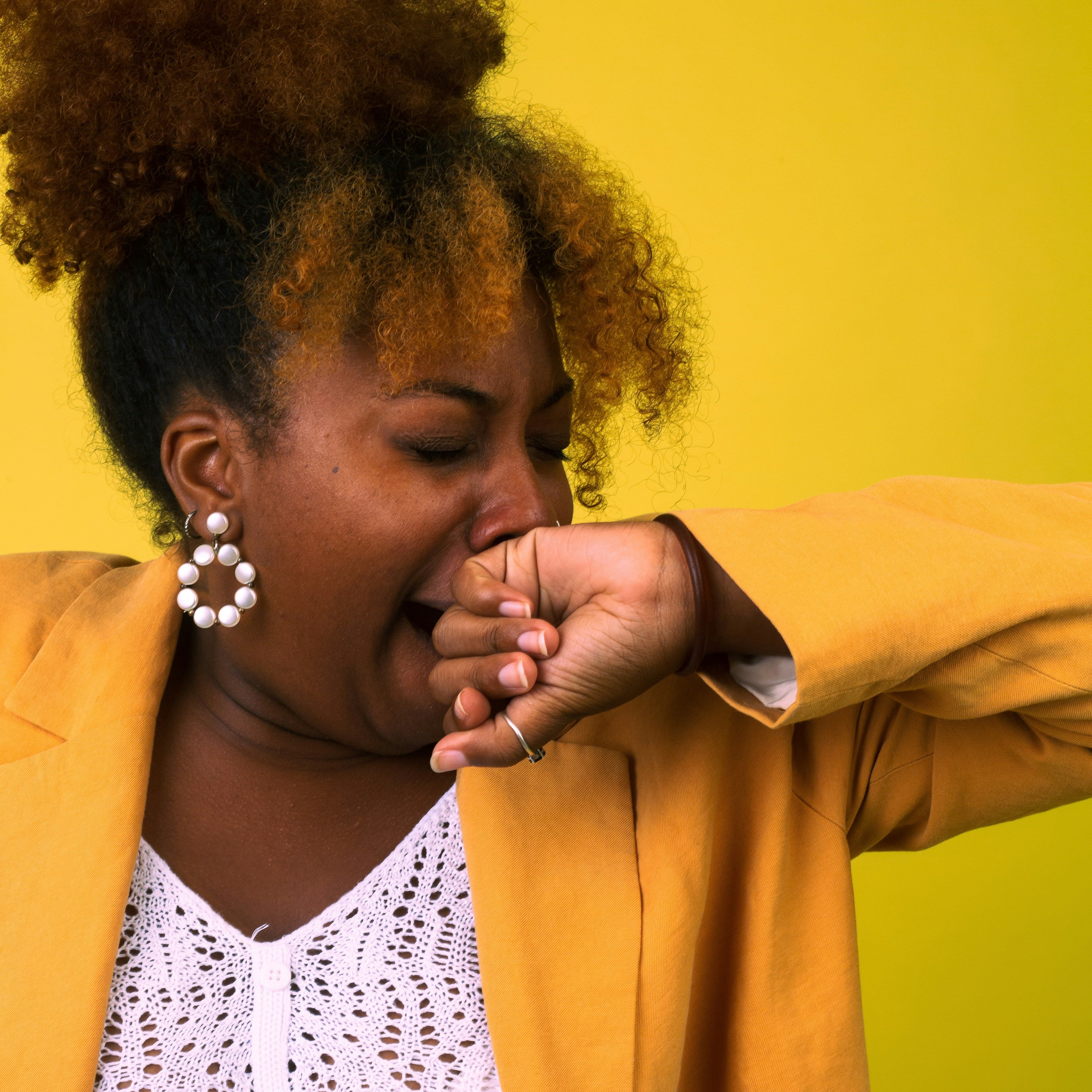 Woman in a yellow jacket with her hand over her mouth against a yellow background
