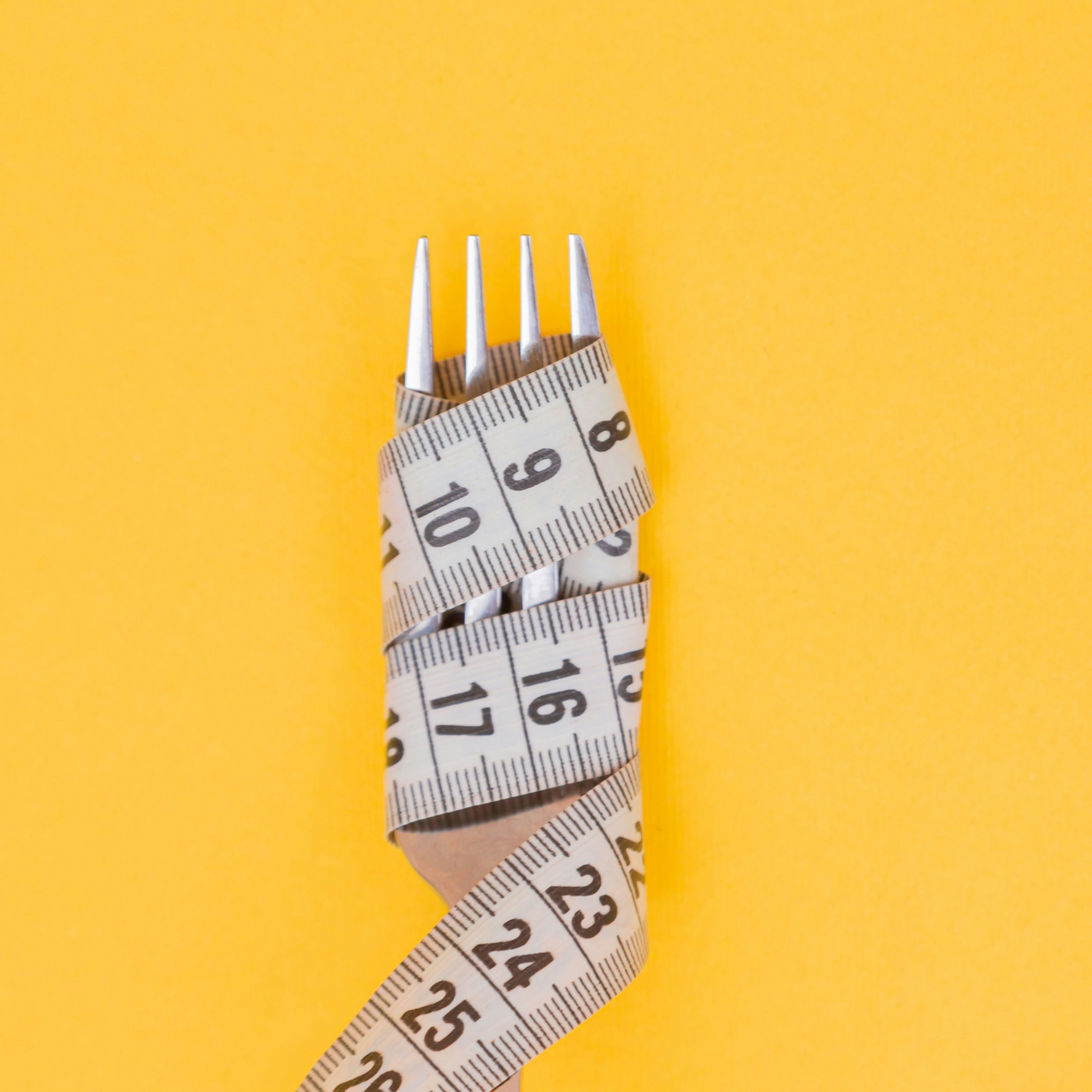 Fork with a measuring tape wrapped around it on a yellow background