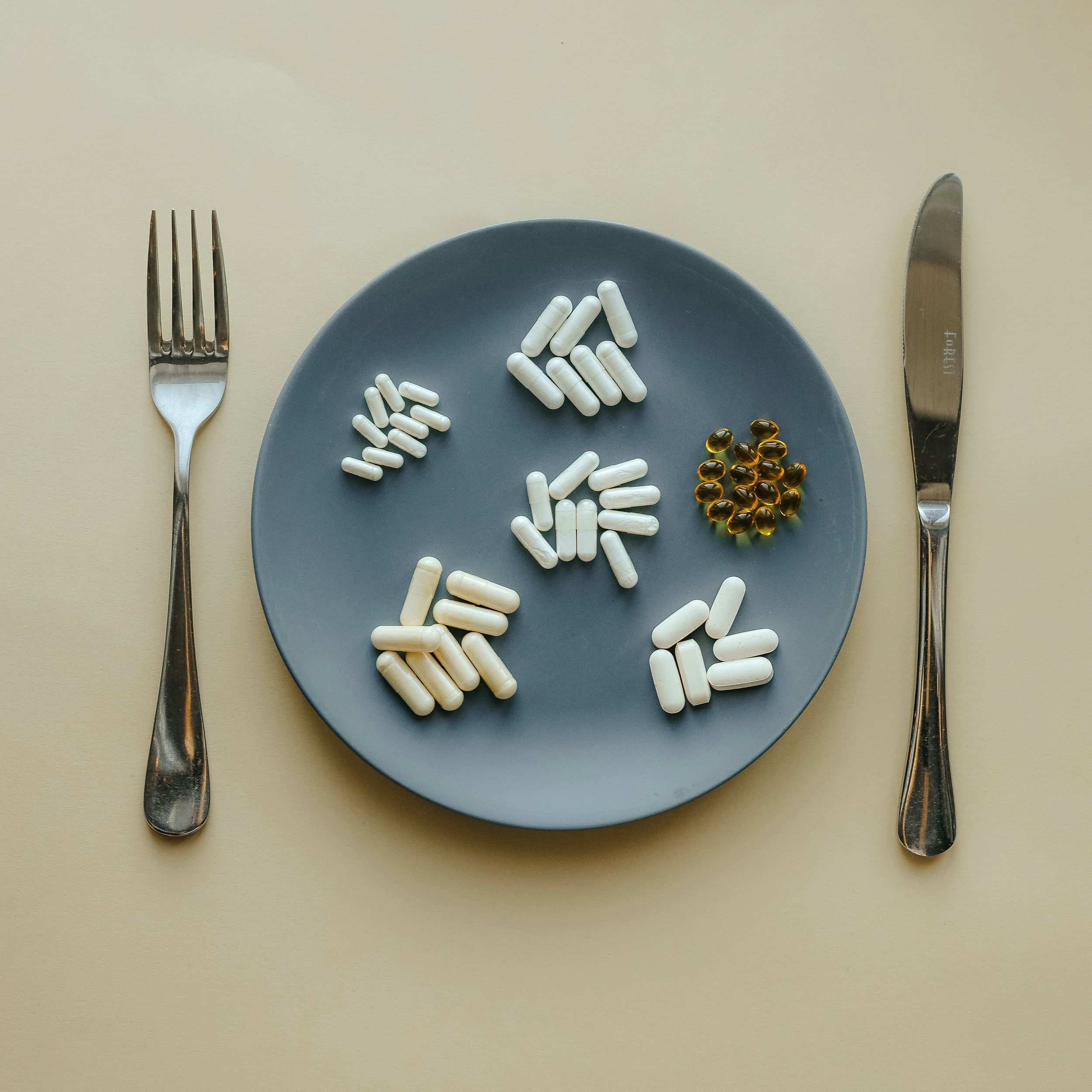 Blue plate with 6 groups of vitamins, a fork, and a knife on a beige background
