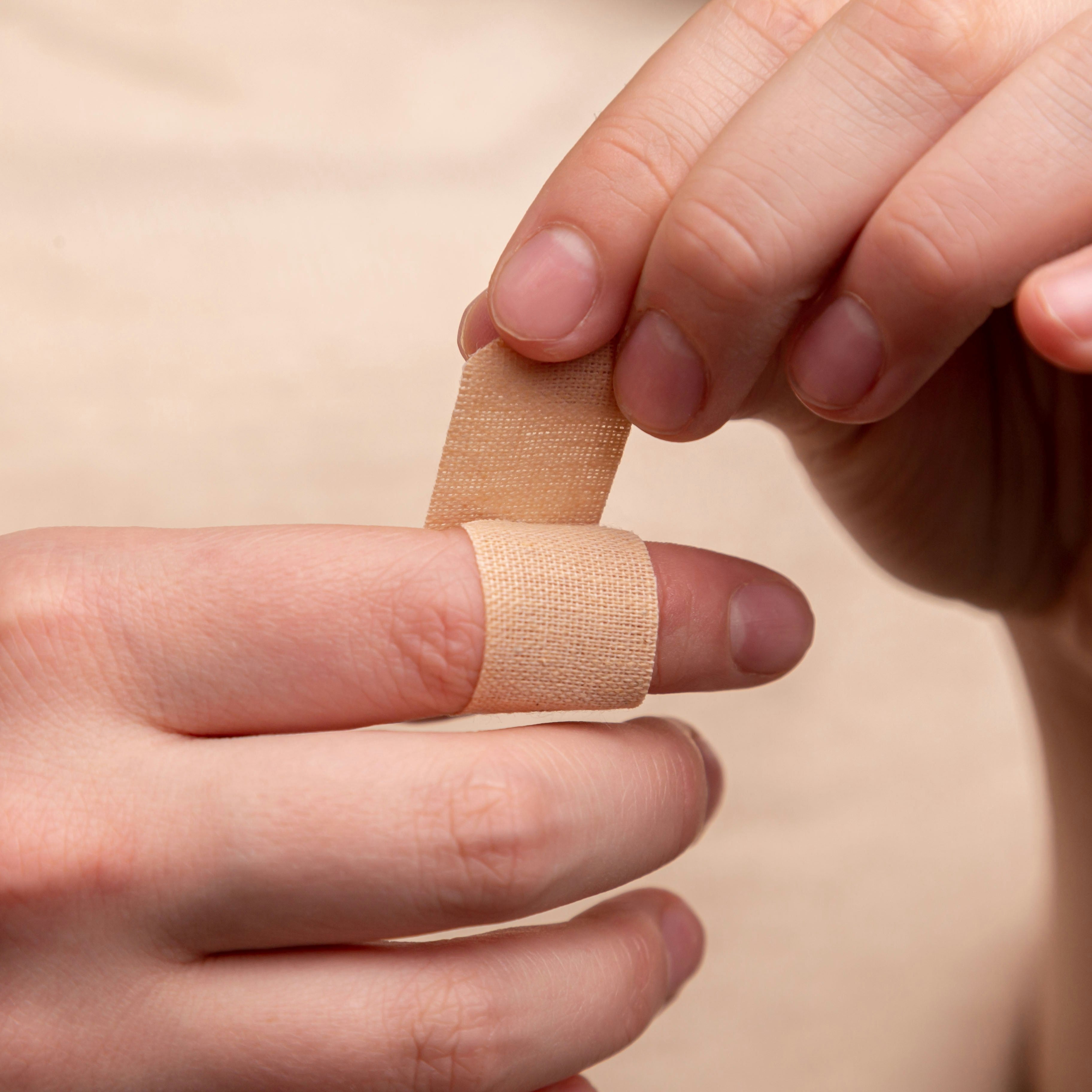 Hand applying a bandage to another hand on a beige background